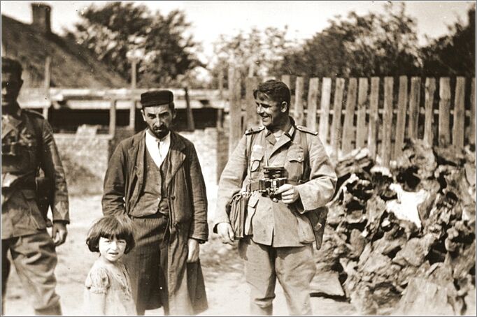 A German soldier with a binoculars laughs at a Polish Jew, who stands with his young daughter in Czestochowa